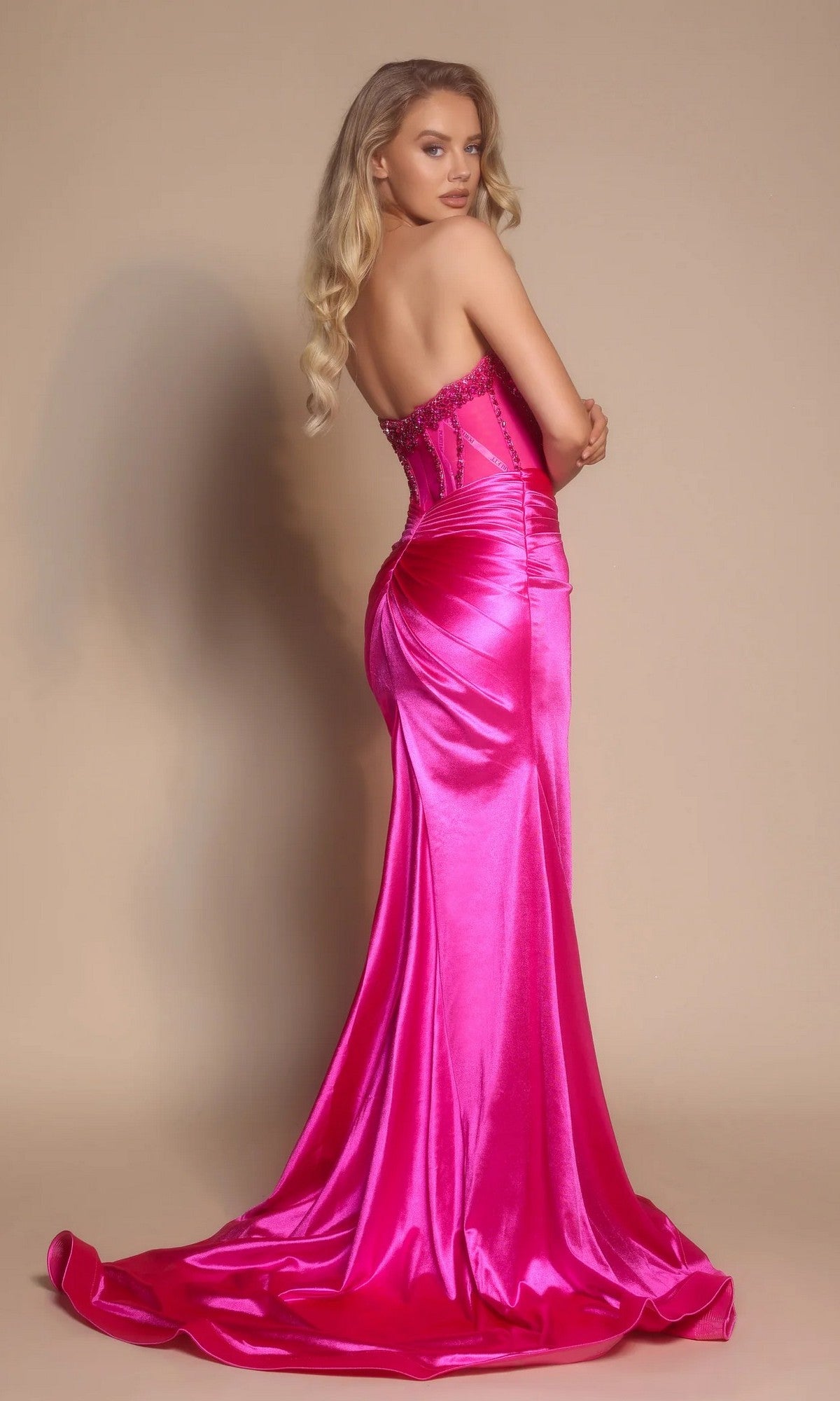A woman with long blonde hair models the Portia and Scarlett PS26073, a strapless formal dress with a beaded bodice and fitted hot pink satin skirt with train, against a plain beige background.